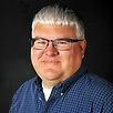 A man wearing glasses and a blue shirt is smiling for the camera.