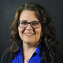 A woman wearing glasses and a blue shirt is smiling for the camera.