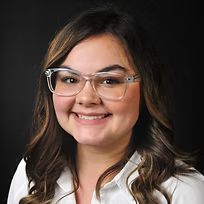 A woman wearing glasses and a white shirt is smiling for the camera.