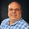 A bald man wearing glasses and a plaid shirt is smiling for the camera.