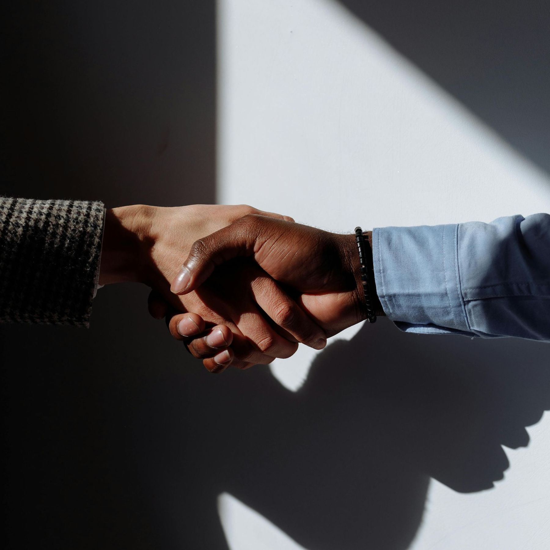 Two people are shaking hands in front of a white wall.
