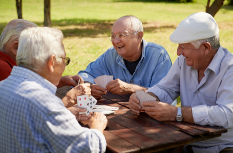 A group of older men playing cards at a picnic table.