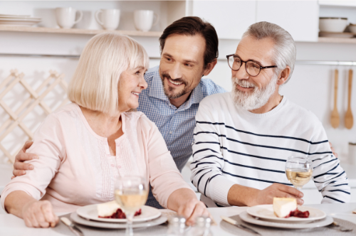 A picture of an older couple eating with a man standing behind him.