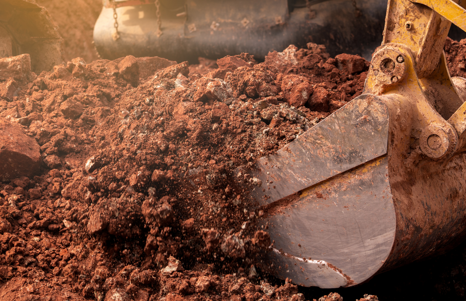 Excavator bucket filled with red-brown soil, close-up view.