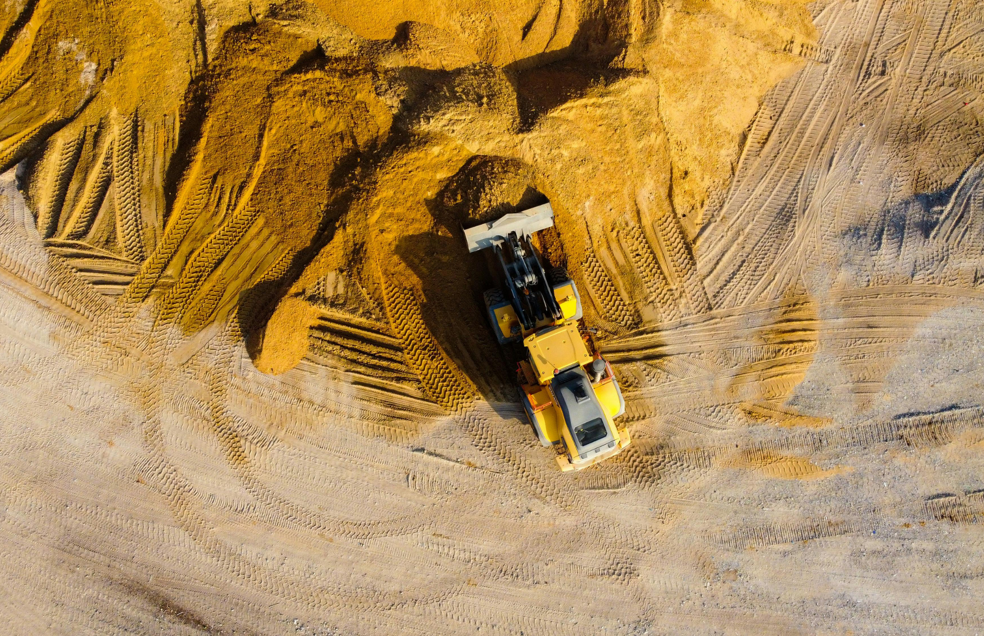 Yellow loader on a sand pile, creating patterns. Top-down view.