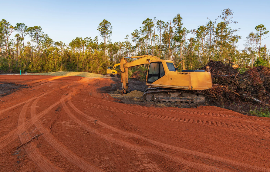 Yellow bulldozer on red dirt at a construction site, with a tree line in the background..