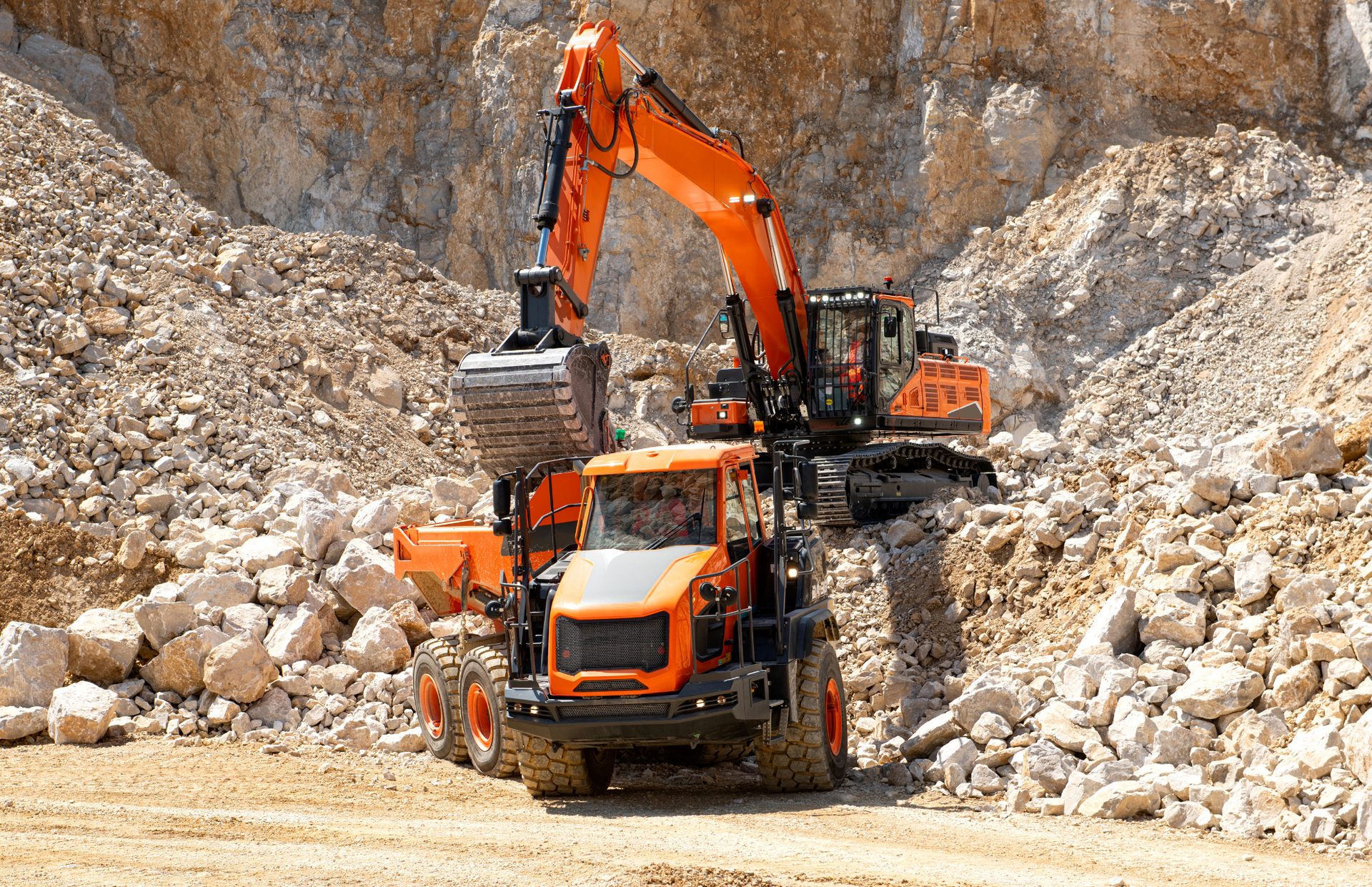 Excavator loading a dump truck with rocks in a quarry; orange machinery.