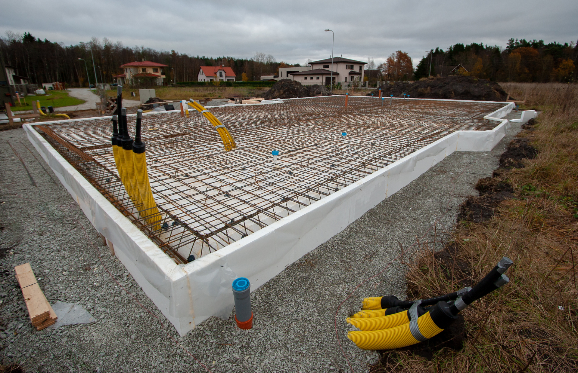 Construction workers on a concrete base, inspecting and working with metal rods, wearing safety vests and helmets.