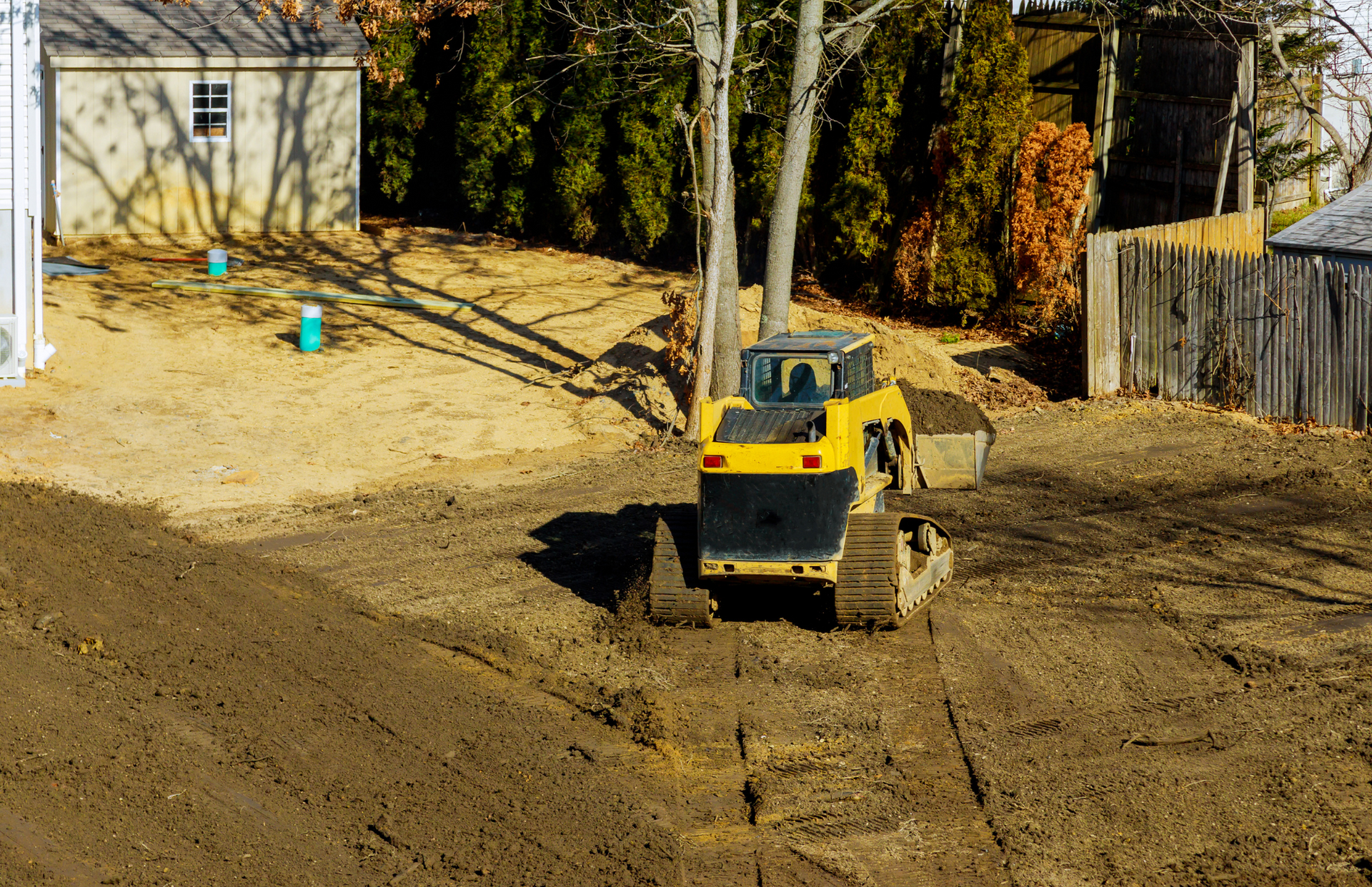 Yellow skid steer operating on dirt, preparing a yard for landscaping.