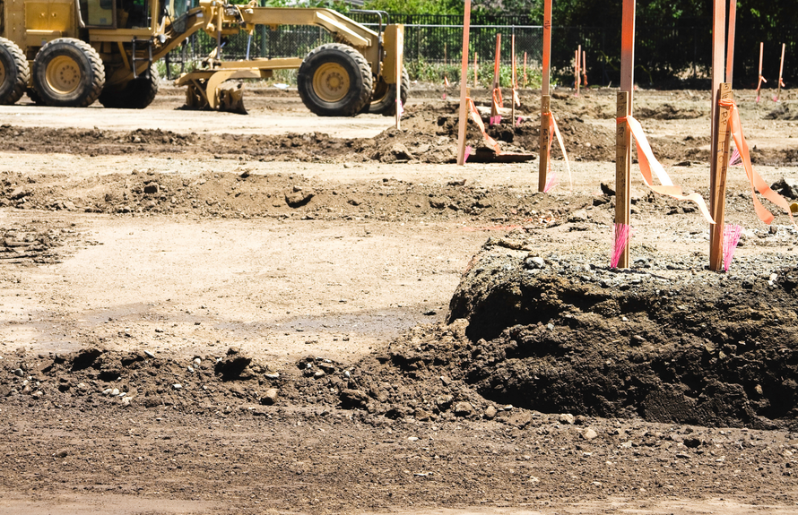 Yellow front-end loader on a construction site, moving yellow material, creating textured patterns in sand.