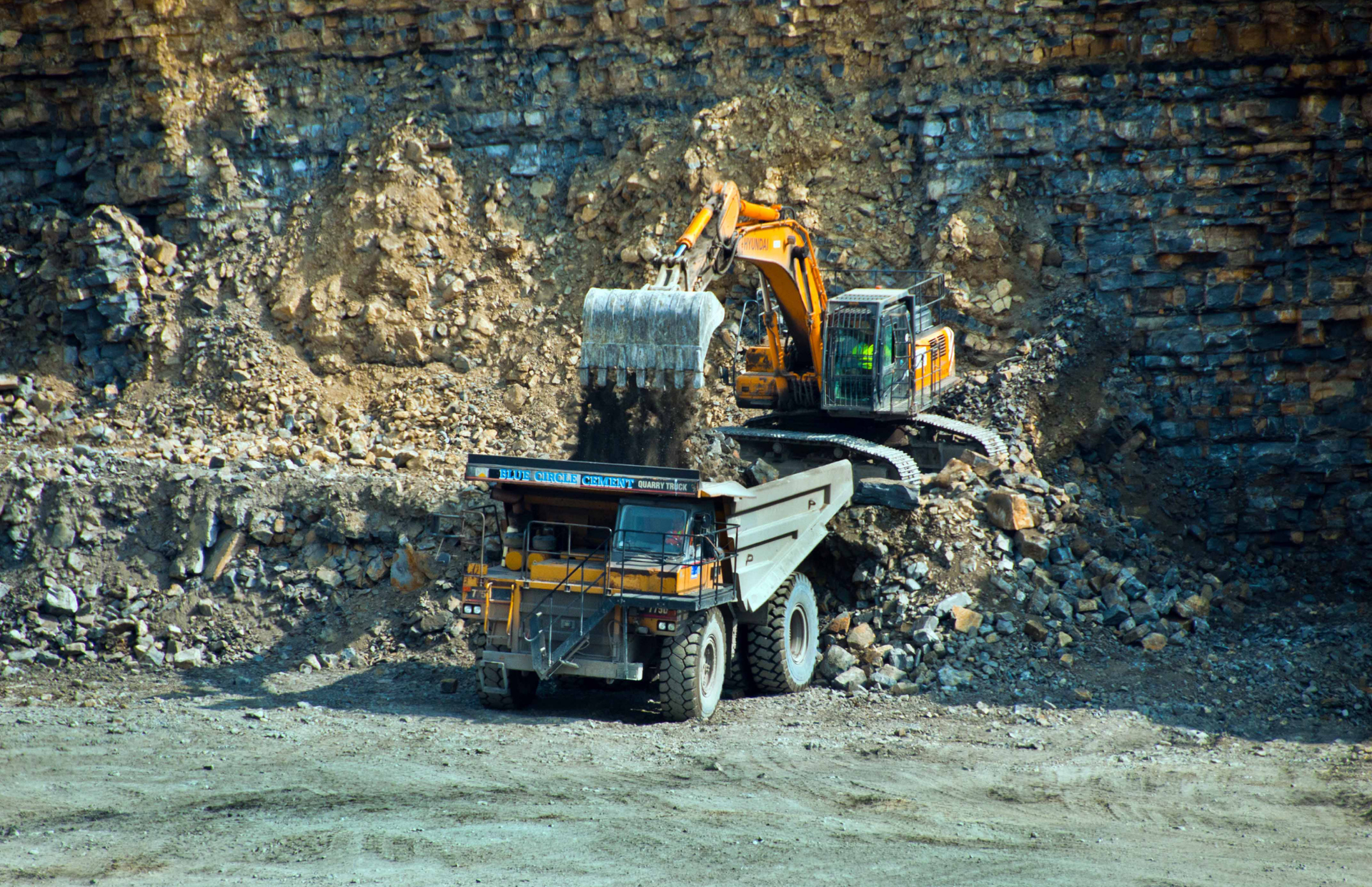 Excavator loading a dump truck with rocks in a quarry; orange machinery.