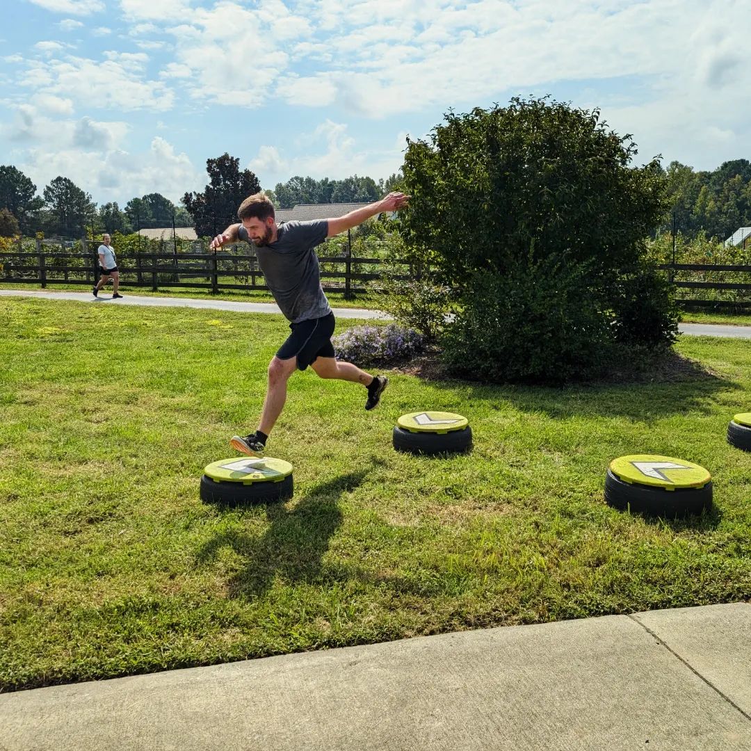 Man jumping between circular platforms on grass, another person walking on path in background.