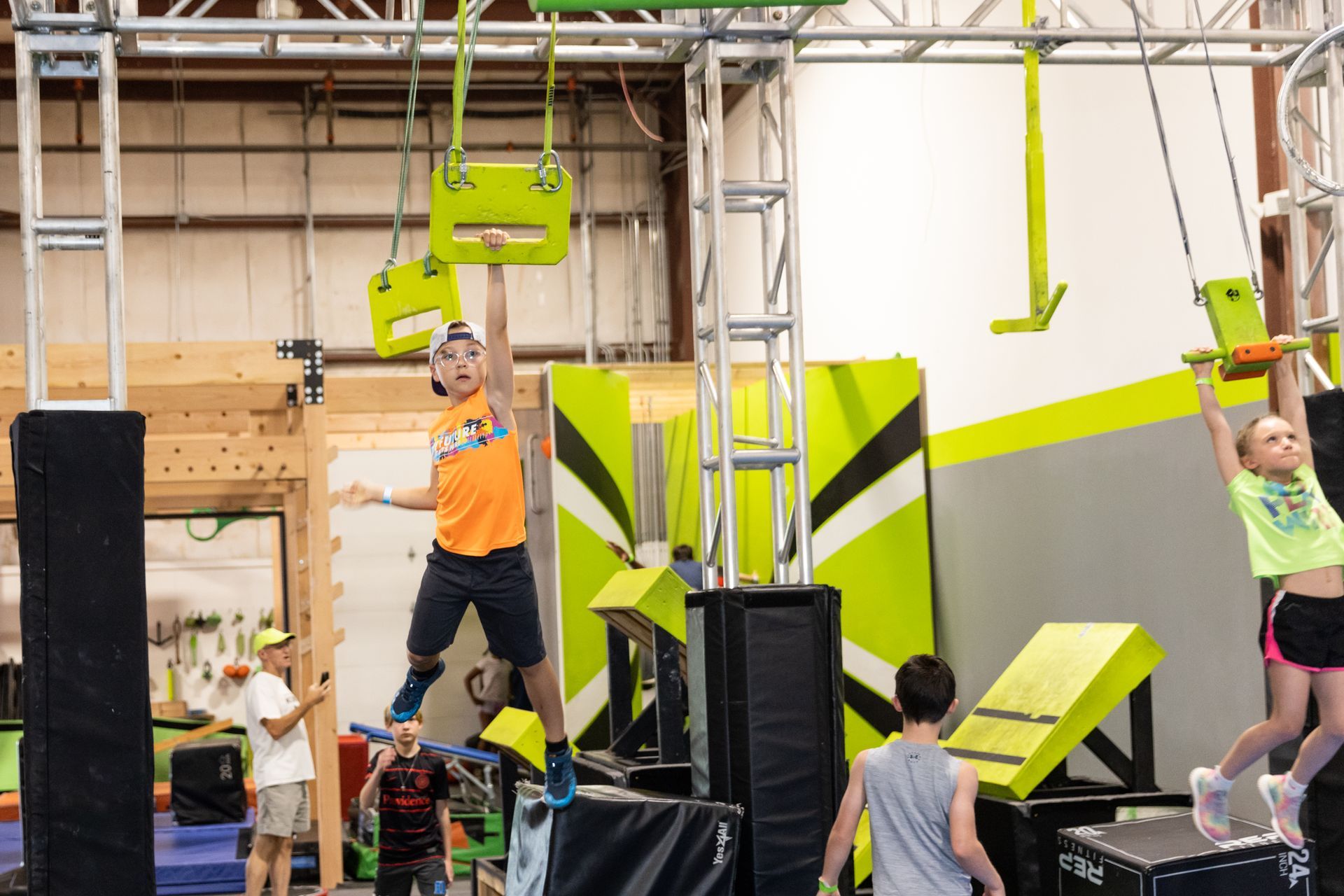 Children on an indoor obstacle course, hanging from bars. Bright colors, active setting.