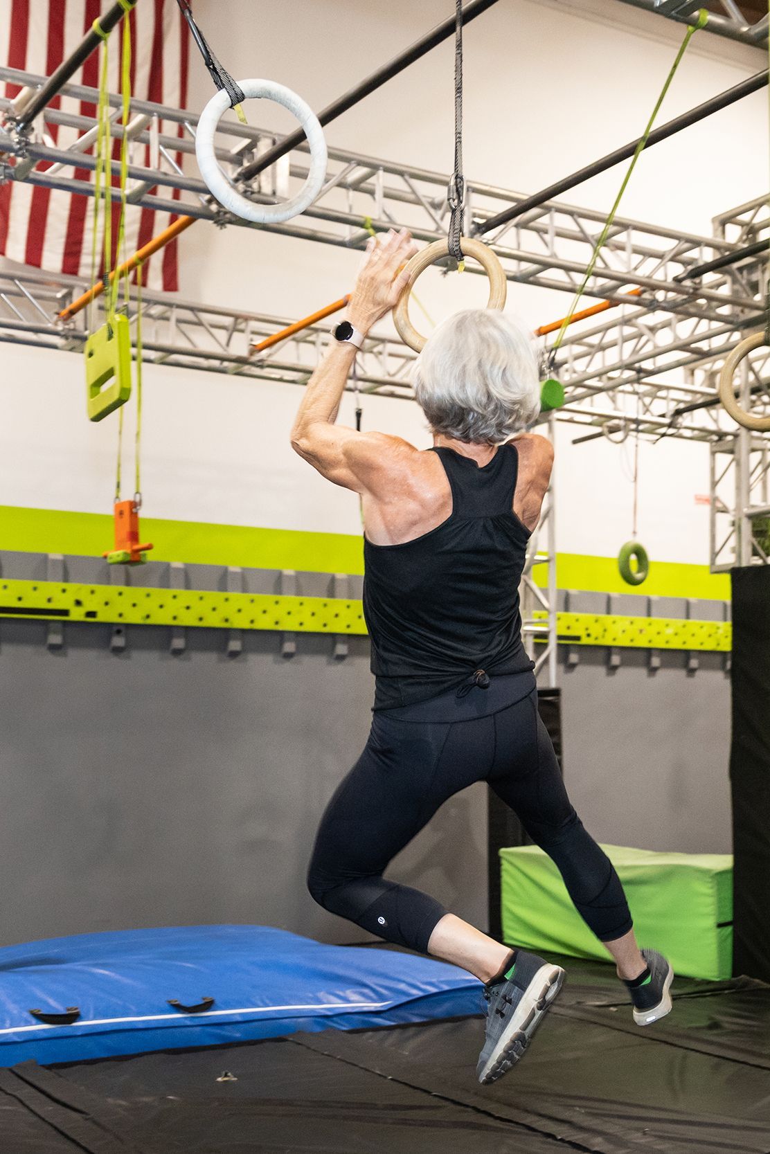 Woman in black activewear on gymnastic rings at an indoor gym.