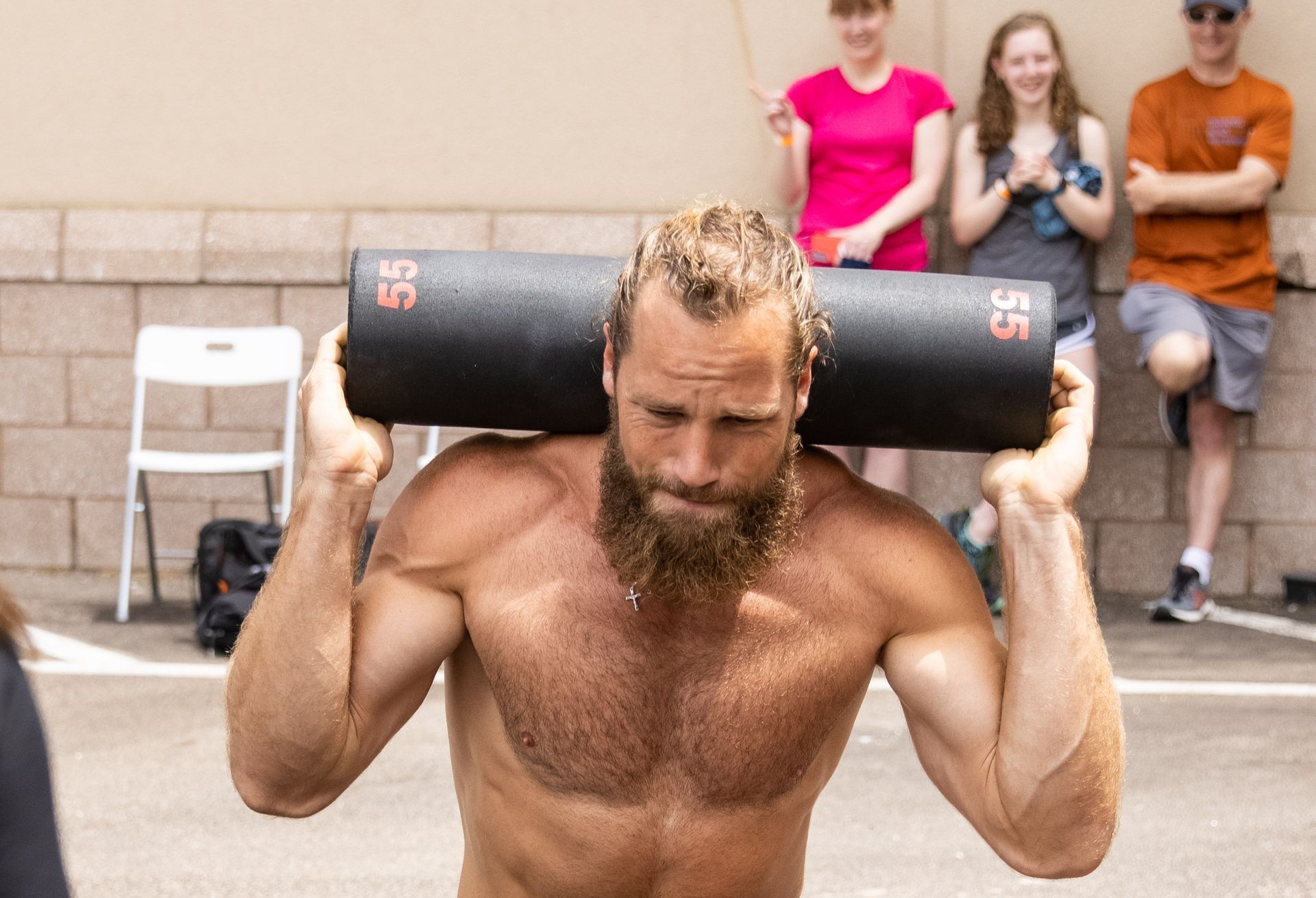 A shirtless man with a beard is carrying a black bag on his shoulders.