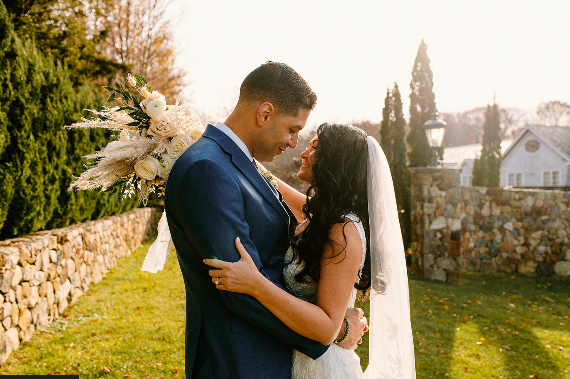 Wedding couple embraces outdoors, bride in veil, groom in blue suit, holding bouquet at The Whittemore.