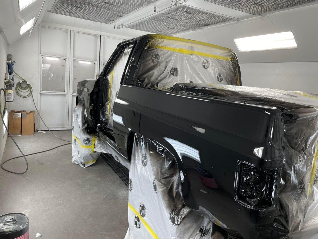 A black truck is being painted in a paint booth. | B & K Collision