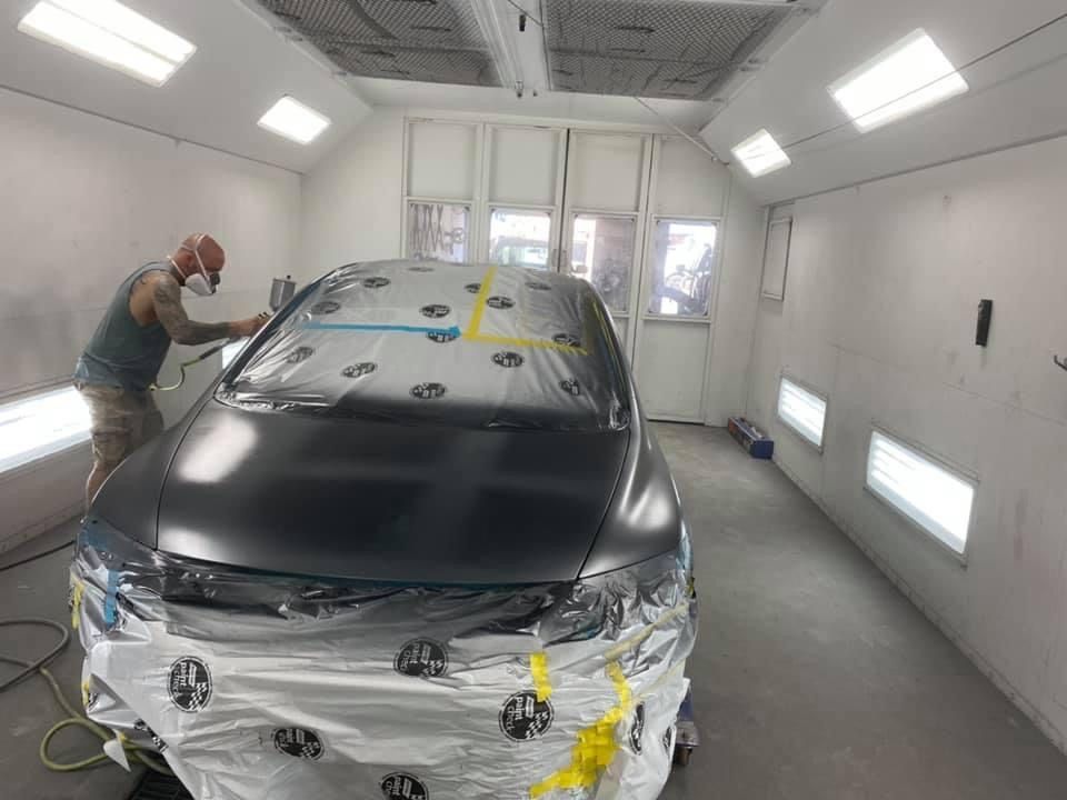 A man is painting a car in a paint booth. | B & K Collision