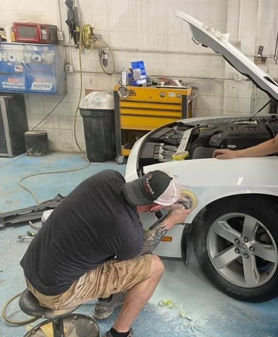 A man is kneeling down polishing a car in a garage. | B & K Collision