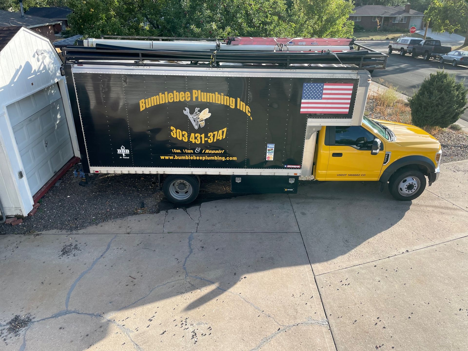 A yellow plumbing truck is parked in a driveway next to a garage.