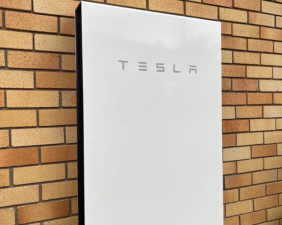A Tesla Powerwall Mounted On A Brick Wall — Efficient Solar Panels in Armidale