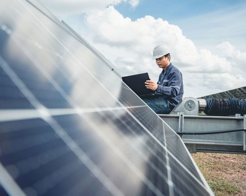 A Man Sitting On Top Of A Solar Panel Using A Laptop — Experienced Solar Installers in Tamworth