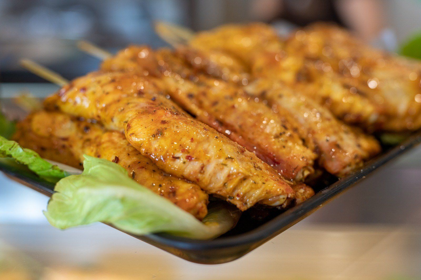 Una persona tiene in mano un vassoio di ali di pollo infilzate su degli spiedini.