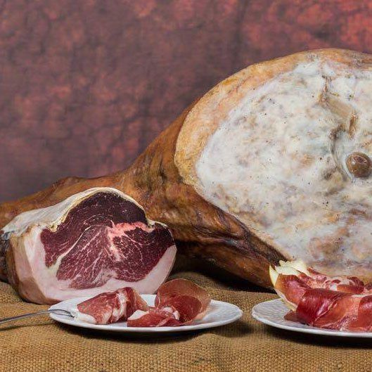 Un grosso pezzo di prosciutto è appoggiato su un tavolo accanto a due piatti di prosciutto.