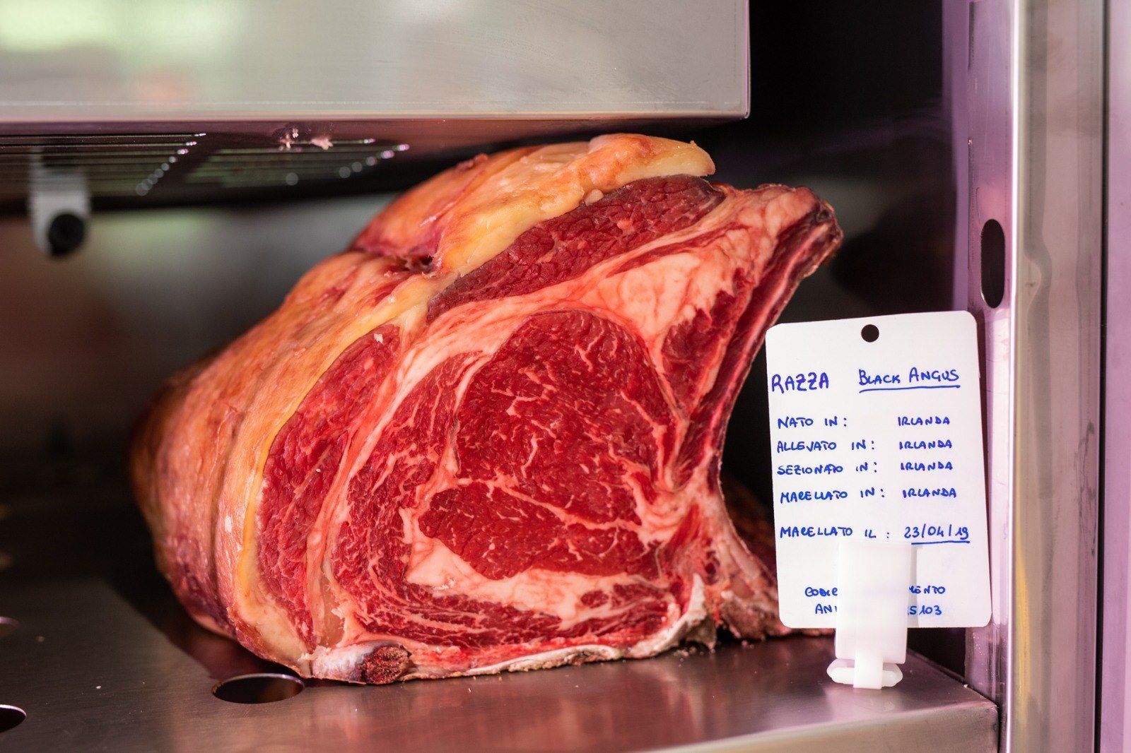 Un grosso pezzo di carne è appoggiato su uno scaffale accanto a un cartellino del prezzo.