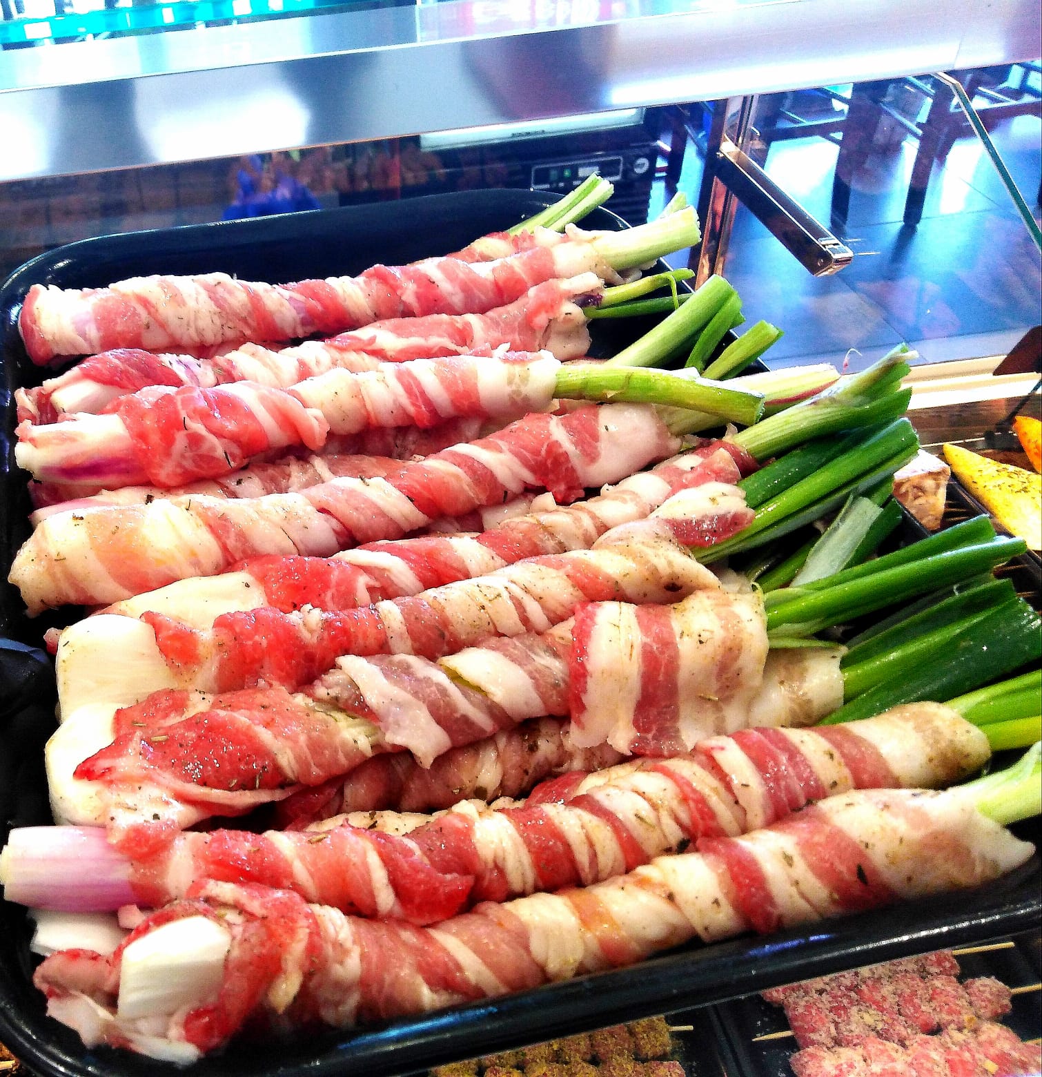 Un vassoio di carne avvolto in pancetta e cipolle verdi