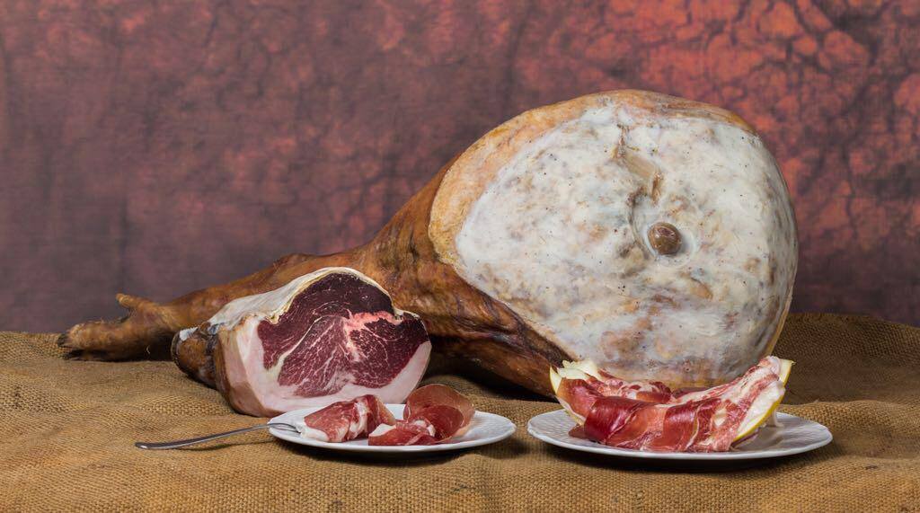 Un grosso pezzo di prosciutto è appoggiato su un tavolo accanto a due piatti di prosciutto.