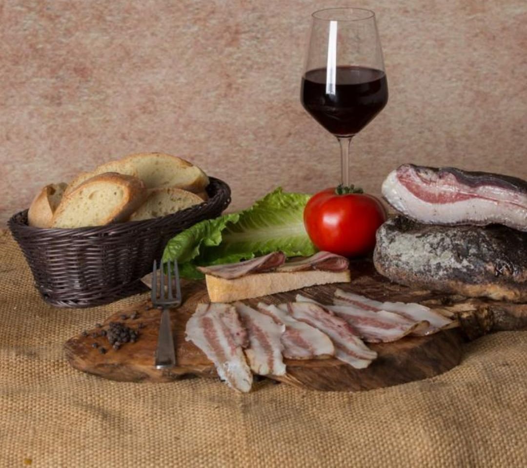 Un tagliere di legno pieno di carne e verdure accanto a un bicchiere di vino