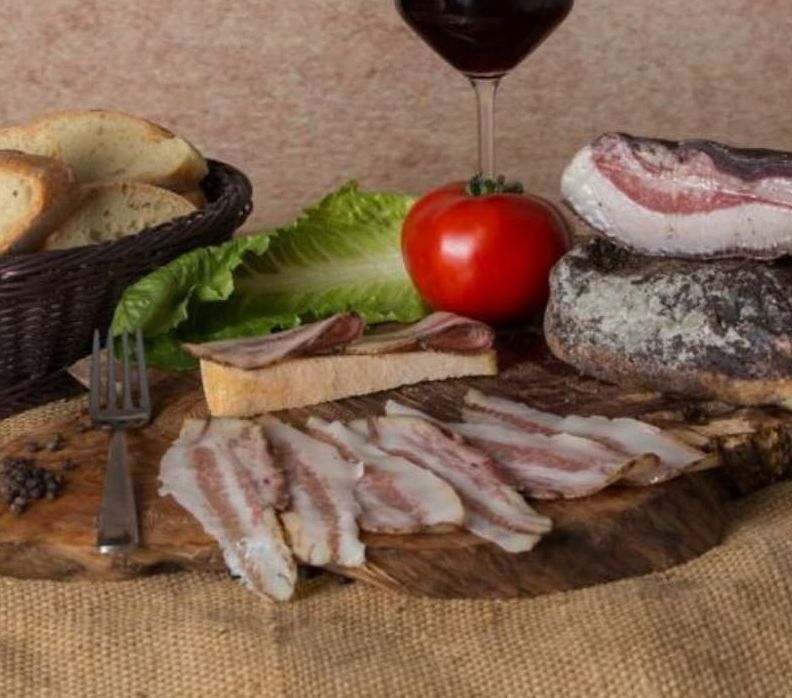 Un tagliere di legno con pancetta, pomodori e un bicchiere di vino