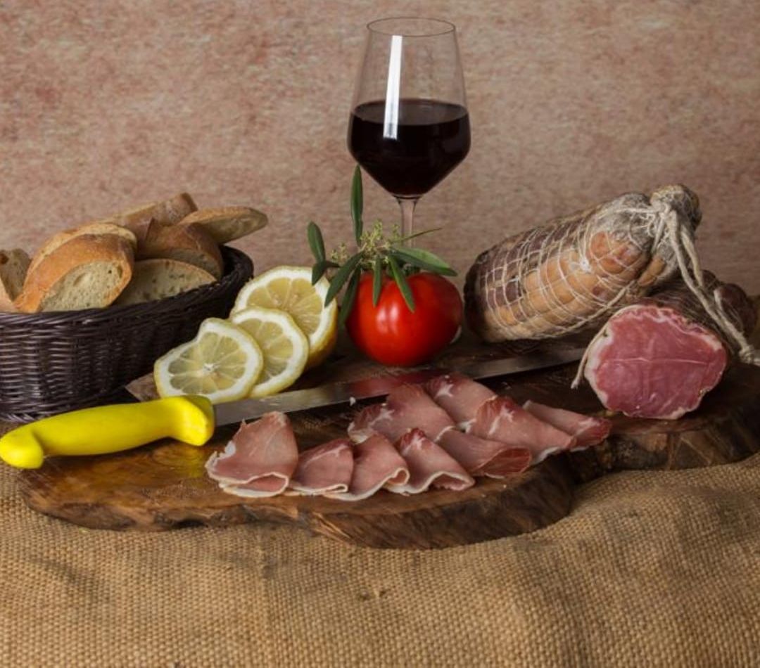 Un tagliere di legno pieno di carne e verdure accanto a un bicchiere di vino