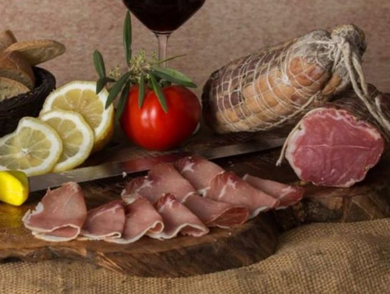 Un tagliere con carne affettata, pomodori, limoni e un bicchiere di vino