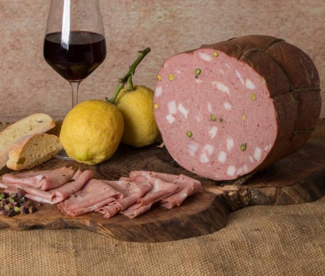Un grande pezzo di carne è appoggiato su un tagliere di legno accanto a limoni e un bicchiere di vino