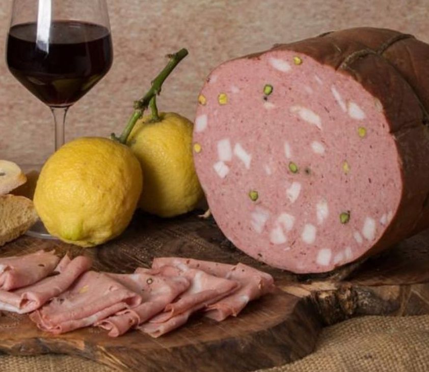 Un grosso pezzo di carne è appoggiato su un tagliere di legno accanto a dei limoni e un bicchiere di vino.