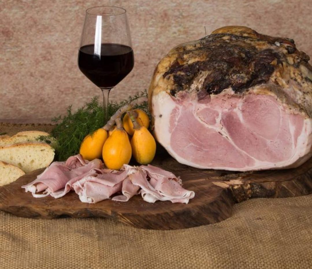 Un grande pezzo di prosciutto è appoggiato su un tagliere di legno accanto a un bicchiere di vino