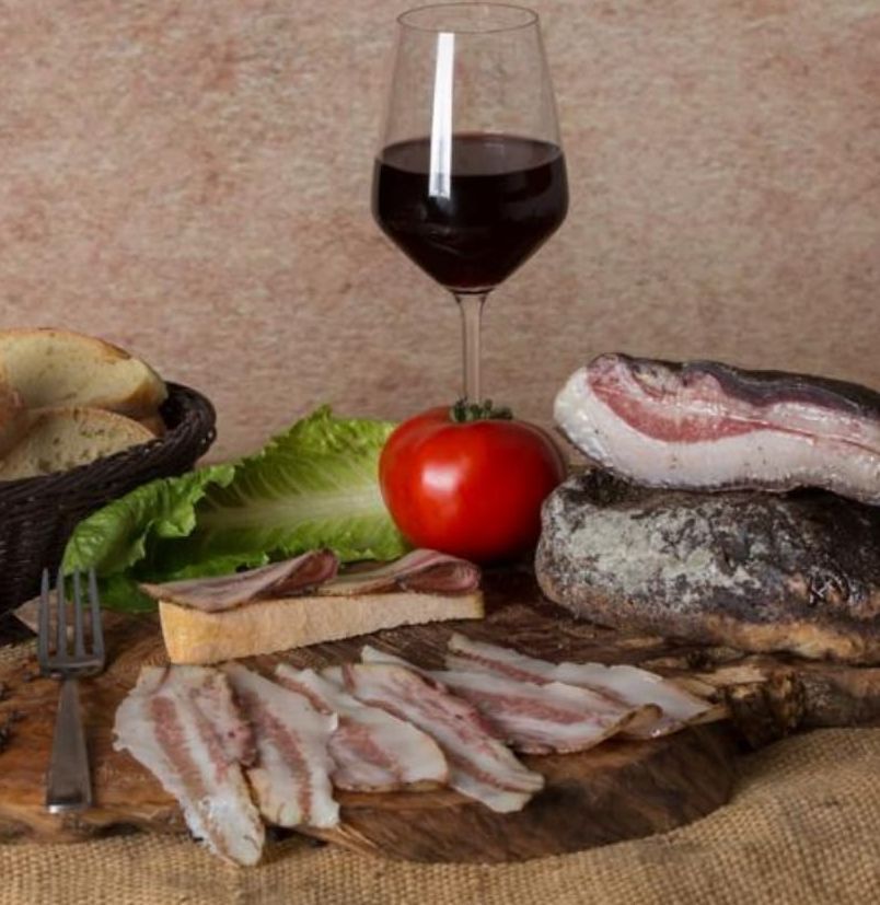 Un tagliere con pancetta, pomodori e un bicchiere di vino