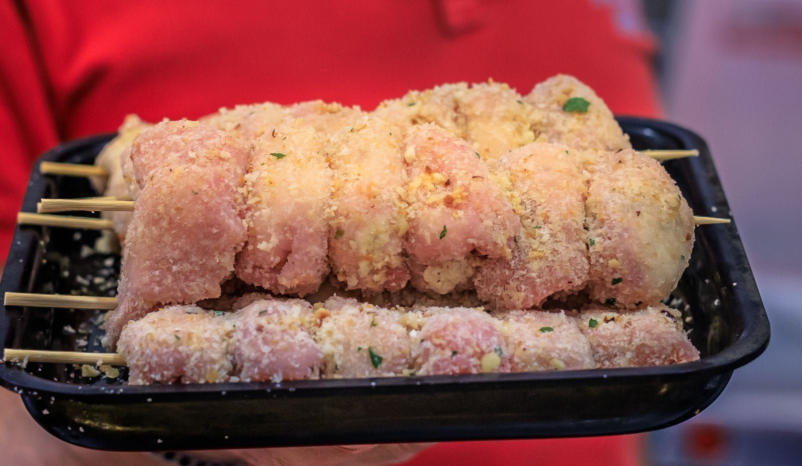 Una persona tiene in mano un vassoio di plastica pieno di spiedini di pollo.