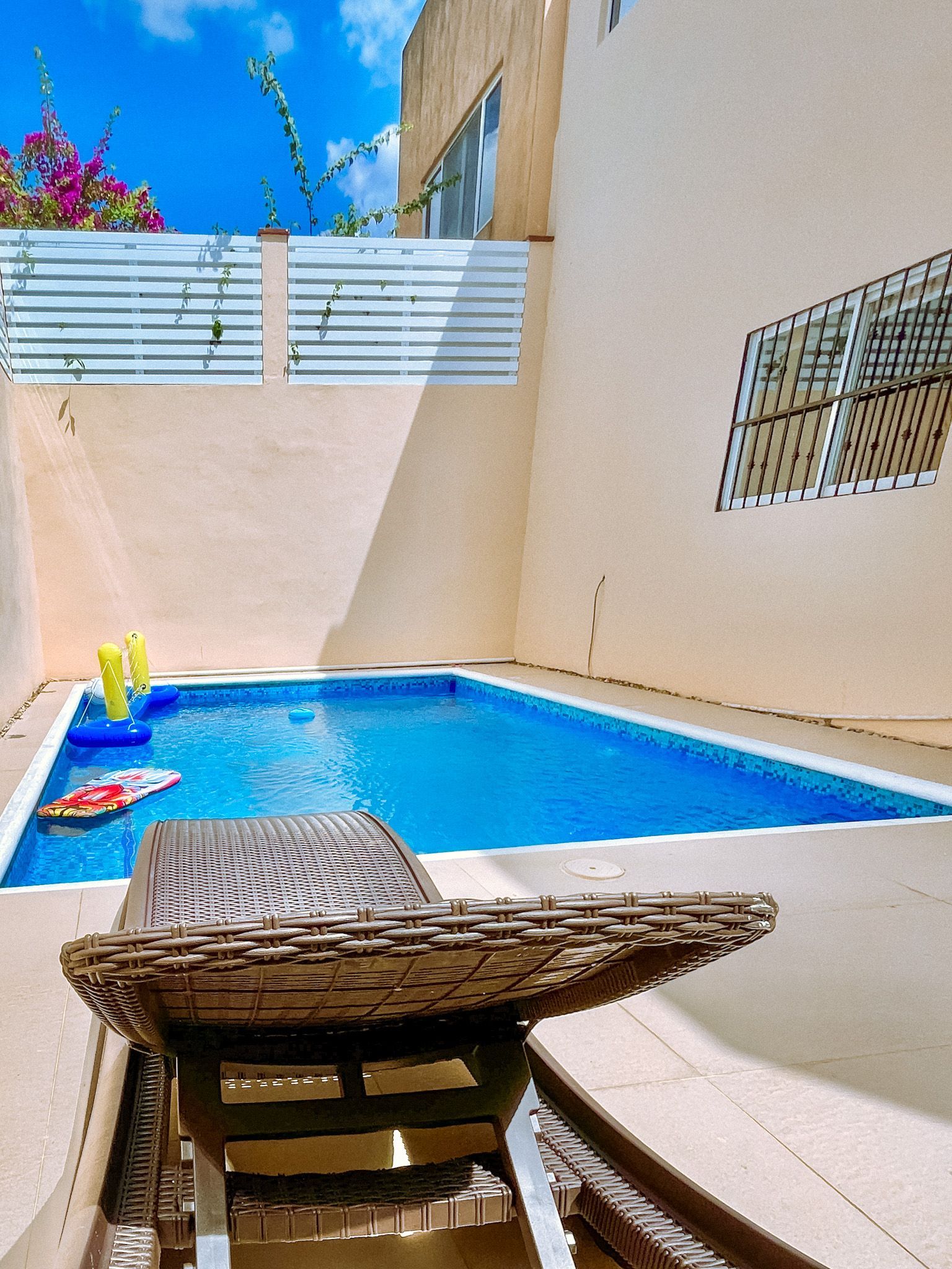 Small pool in a walled yard with lounge chair, clear blue water, sunny sky.