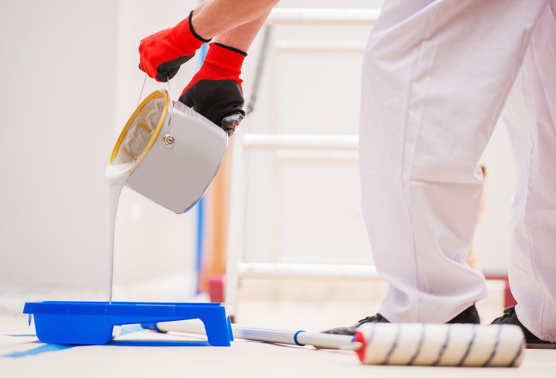 A man is pouring a can of paint in a paint roller tray.