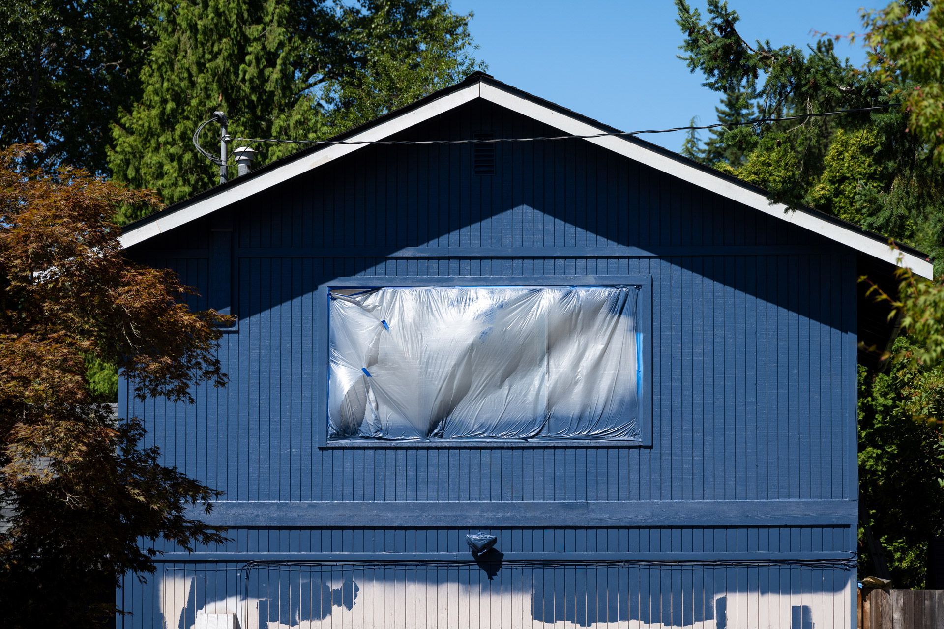 A blue house exterior with a window covered in plastic sheeting during painting work