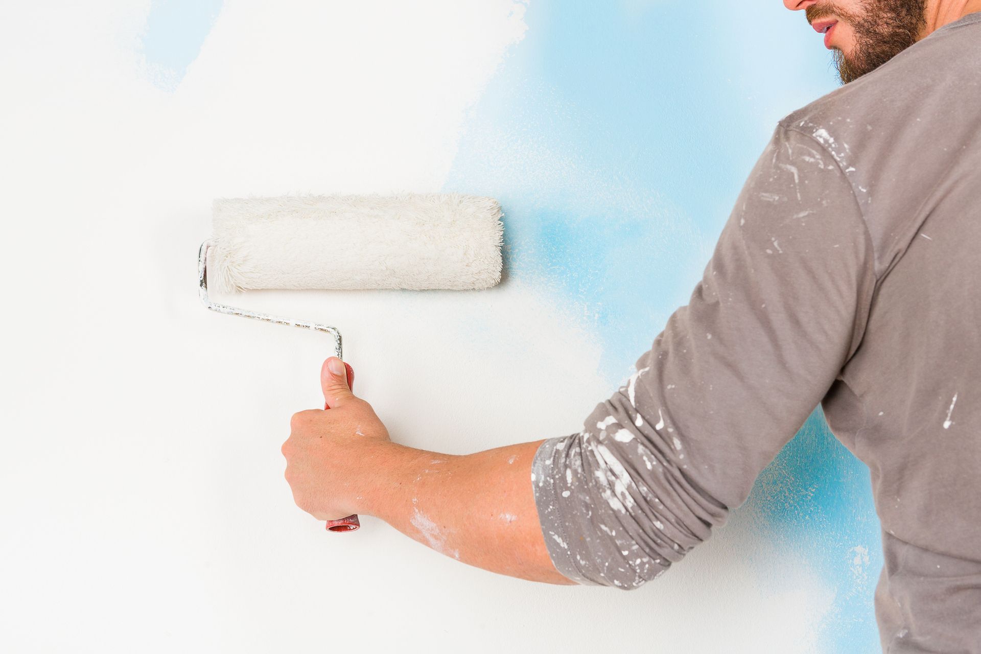 Person painting wall with roller applying white and blue paint during home renovation.