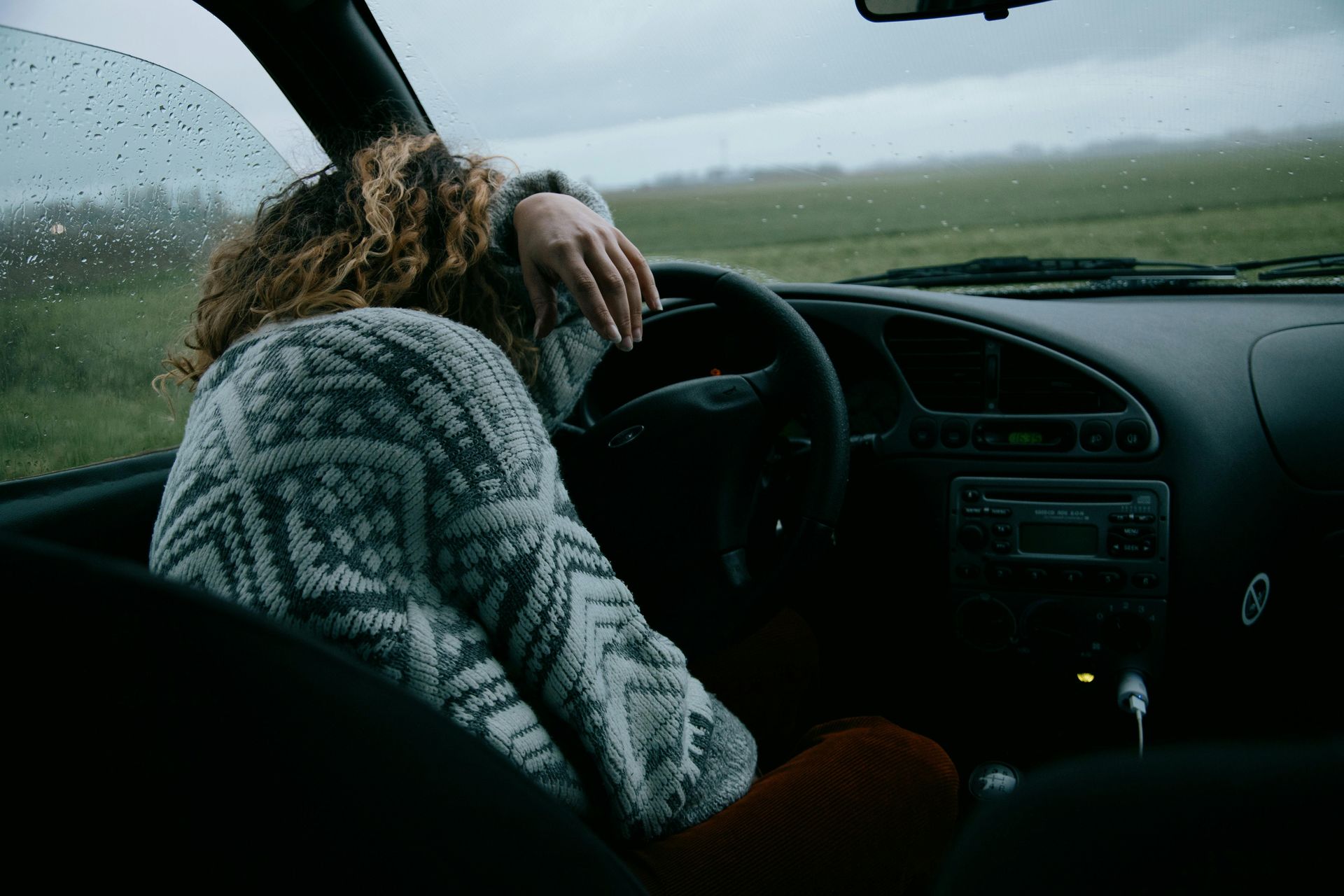 Woman resting head on the steering wheel inside car, showing the increased risk of drowsy driving