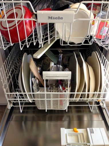 Open dishwasher with dishes, bowls, and utensils stacked inside wire racks.