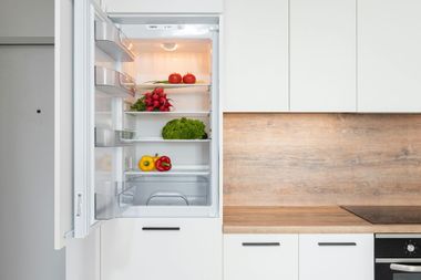 Open refrigerator in a white kitchen with fresh produce on shelves