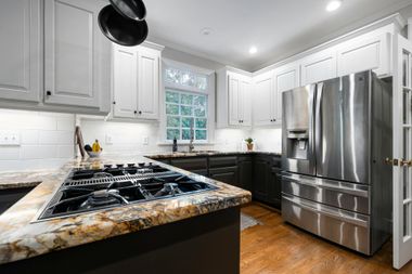 Modern kitchen with white cabinets, black granite island, stainless steel appliances, and wood floors