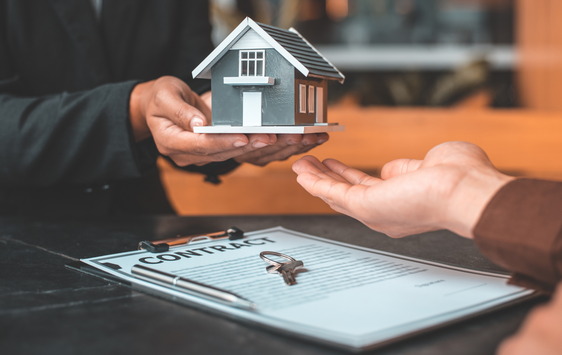 A person is holding a model house in their hands over a clipboard.