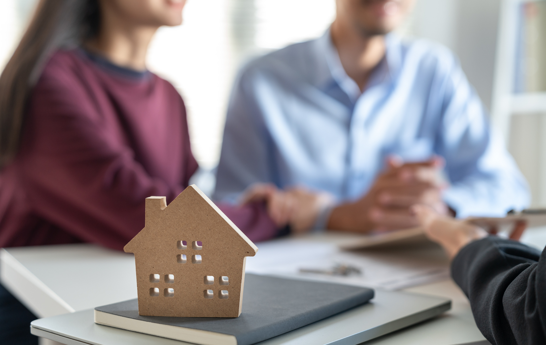 A couple is sitting at a table with a model house on top of a book.